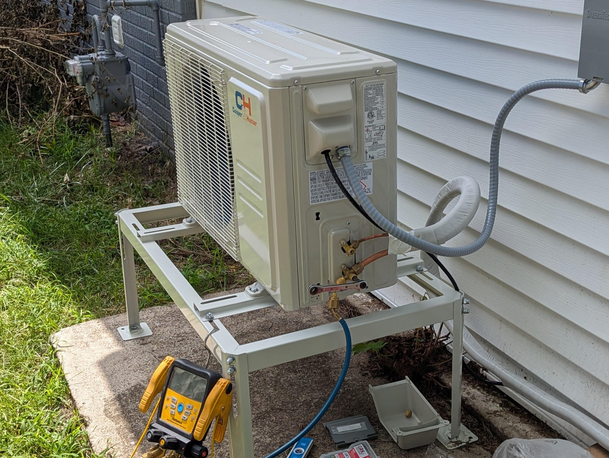 Outdoor condenser raised on a metal equipment stand beside siding