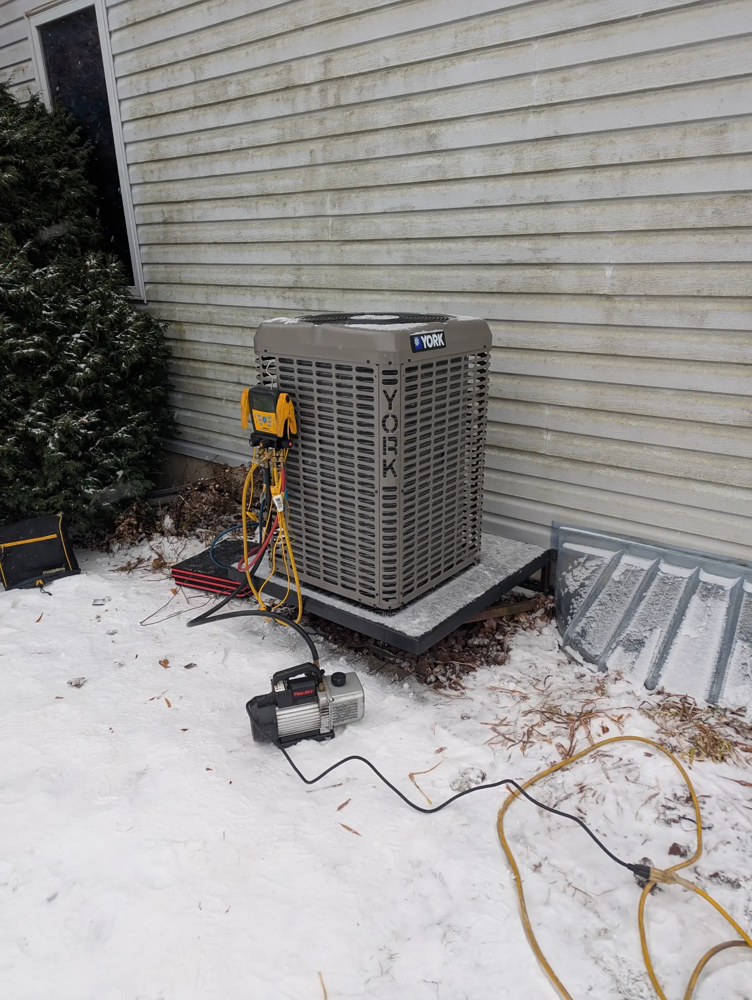 Outdoor HVAC condenser beside a snow-covered residential wall